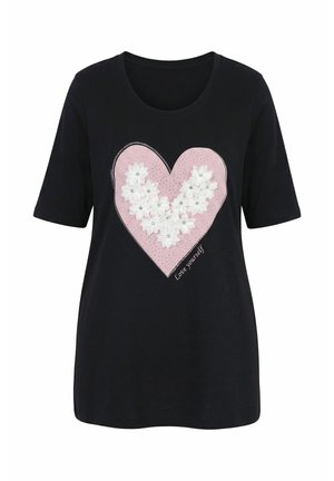 T-shirt noir à manches courtes avec un grand cœur rose décoré de fleurs en tissu blanches et de strass, texte "Aime-toi" en bas à droite.