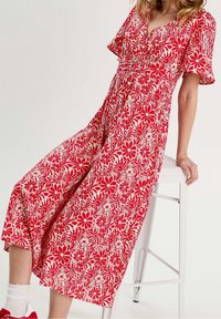 Robe portefeuille rouge à fleurs avec manches courtes, décolleté en V et jupe jusqu'au genou. Le tissu présente un motif floral audacieux et répétitif.