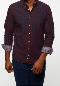 Camisa de hombre de manga larga en rayas rojo oscuro y azul marino, con puños de contraste en un patrón. Presenta un frente abotonado y un diseño ajustado.