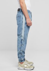 Blugi din denim de culoare albastru deschis, cu o croială ajustată, având o dunga laterală contrastantă de culoare albastru deschis și capse pe picior.