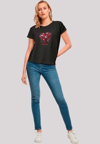 Black short-sleeve t-shirt featuring a colorful heart tree design. Paired with blue skinny jeans and white sneakers.