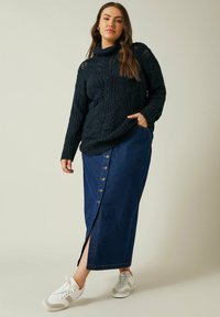 Navyfarbener Strick-Turtleneck-Pullover mit Texturmuster, kombiniert mit einem langen Jeansrock mit frontaler Knopfleiste und Seitenschlitz, abgerundet mit weißen Sneakern.