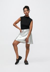 Zwart mouwloos topje, metallic zilveren rok en zwarte platform schoenen. Gladde textuur op de rok, eenvoudig ontwerp, tot aan de knieën, strakke taille.