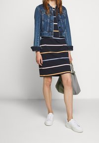 Jeansowa kurtka nałożona na granatową sukienkę w poziome paski w pastelowych kolorach. Białe trampki i jasnoszara torba dopełniają stylizację.