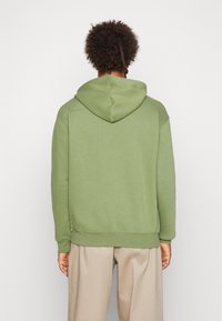 Felpa verde realizzata in tessuto morbido, con cappuccio regolabile tramite cordino, polsini e orlo a coste. Design semplice senza motivi o accenti visibili.