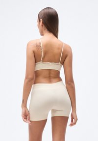Soutien-gorge beige orné de dentelle avec bretelles réglables, associé à un short assorti sans coutures. Texture lisse, coupe ajustée sans motifs visibles.