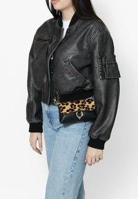 Zwarte leren bomberjack met ribgebreide manchetten, gecombineerd met een kleine crossbody tas met le leopard print, die een zwarte basis en gouden hardware heeft.