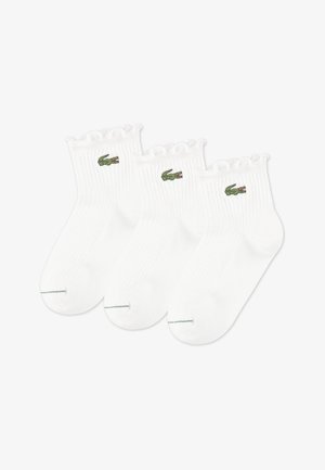 Baltos medvilninės kulkšnies kojinės su ribotu raštu ir banguotais kraštais. Šonuose yra mažas žalias krokodilo logotipas. Pakuotėje yra trys poros.