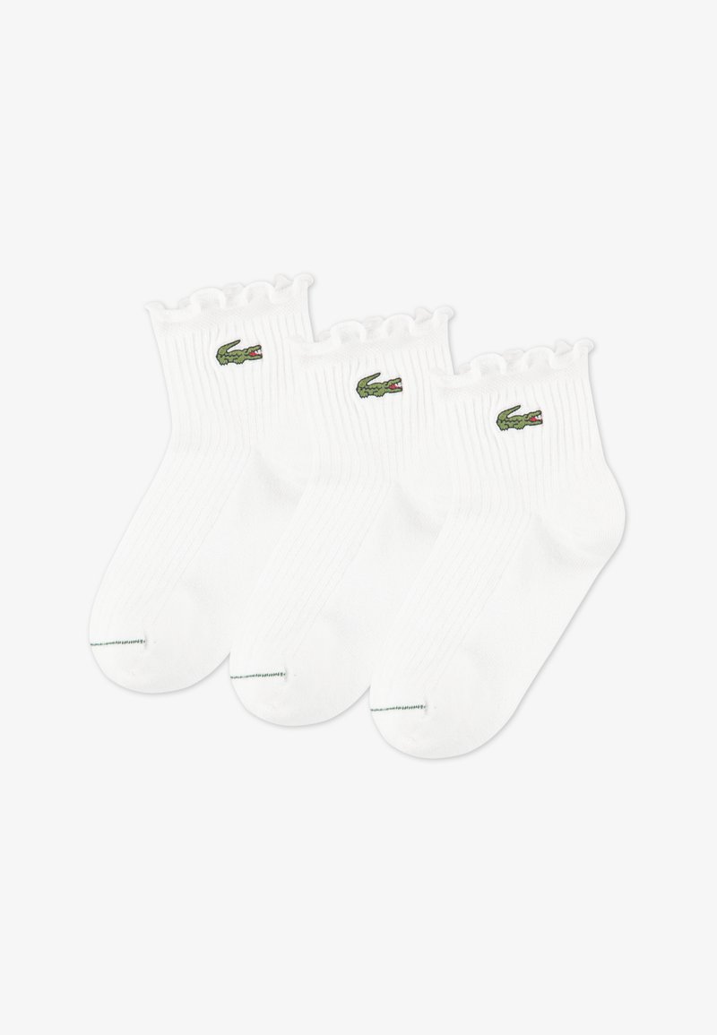 Λευκά βαμβακερά καλτσάκια μέχρι τον αστράγαλο με ριμπ υφή και σκάλιστες μανσέτες. Διαθέτουν μικρό πράσινο λογότυπο κροκόδειλου στα πλάγια. Πακέτο τριών τεμαχίων.