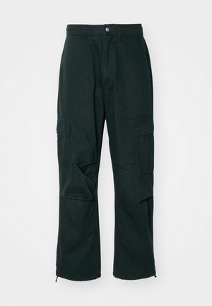 Tumedatest roheline kaubanduslikud püksid, mis on valmistatud vastupidavast kangast, mitmete küljetaskutega, lõdva lõikega ja tõmblukkudega sääreotsades.