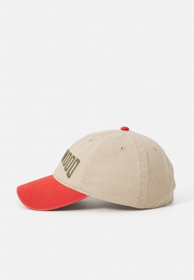 Beige bomullslue med rød skjerm, prydet med grønn tekst foran og en liten rød knapp på toppen. Klassisk sekspanel design.
