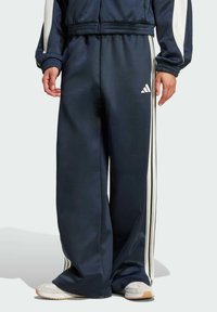 Pantalones de chándal azul marino con rayas blancas en los lados, hechos de tejido suave. Presentan una cintura elástica y un pequeño logo en la parte frontal.