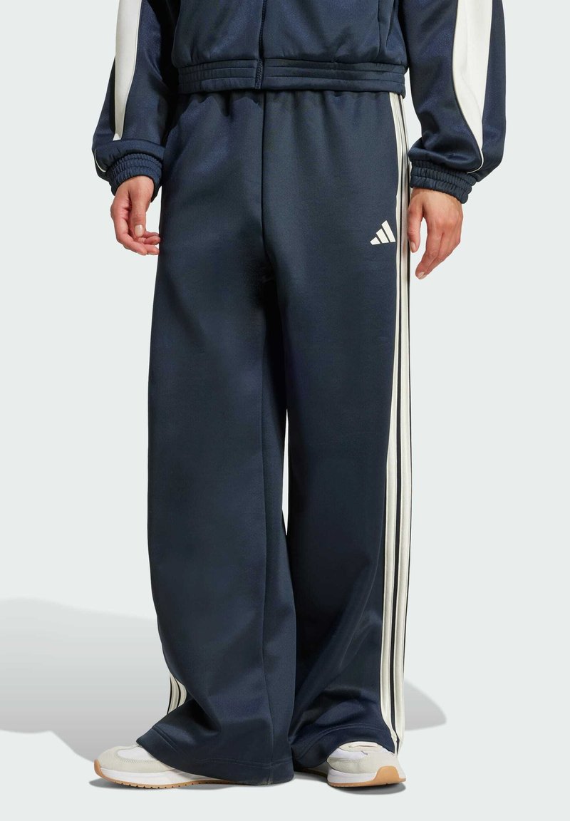 Pantalones de chándal azul marino con rayas blancas en los lados, hechos de tejido suave. Presentan una cintura elástica y un pequeño logo en la parte frontal.