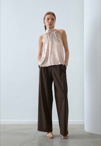 Glänzendes, hellpinker Halftertop mit einer Schleife am Hals, kombiniert mit lockeren, dunkelbraunen weit geschnittenen Hosen und hellbraunen Sandalen.