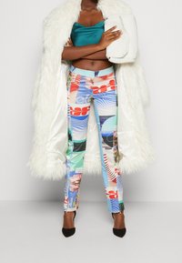 Pantalons imprimés colorés dans diverses teintes, manteau en fausse fourrure blanche, top bleu-vert, et une pochette texturée blanche. Chaussures à talons noirs.