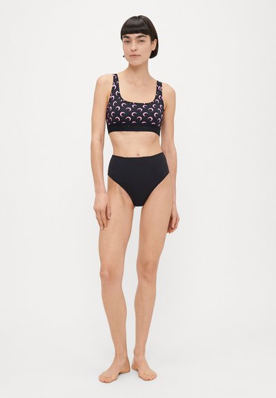 Parte de baixo de biquíni preta de cintura alta combinada com um top desportivo tipo halter com padrão de lua crescente rosa em fundo preto.