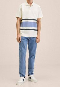 Polo crème à rayures horizontales bleues et marine, associé à un jean bleu clair et des baskets blanches avec des accents marins.