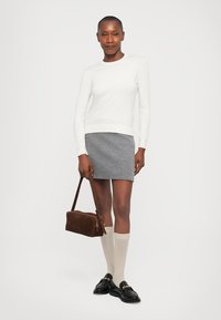 Valkoinen pitkähiha, harmaa villahuovasta tehty mini-hame, kerma väriset polvipituiset sukat, mustat loafers-kengät ja ruskea mokkatuilla laukku.