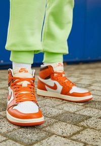 Oranžovo-bílé vysoké tenisky vyrobené z nylonu a kůže, s perforovanou špičkou, oranžovými tkaničkami a značkováním Nike na jazyku.