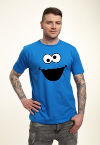 Modrá bavlněná tričko s velkým černobílým obličejem Cookie Monstra. Krátké rukávy a klasický kulatý výstřih.