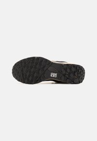 Suela de zapatilla de goma negra con una superficie texturizada que presenta patrones hexagonales para proporcionar tracción. Acentos de color beige claro a lo largo de los bordes.