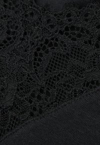 Tela negra con un borde de encaje que presenta patrones y texturas intrincadas. El encaje es delicado, proporcionando un contraste con el material negro sólido de abajo.