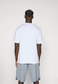 Hvid bomulds T-shirt med rund hals, parret med grå meshsportsbukser med sideslids ved kanten. Kun bagvisning, ingen grafik eller logoer.