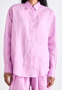 Light pink linen button-up shirt featuring a classic collar, single chest pocket, and long sleeves, paired with matching trousers.