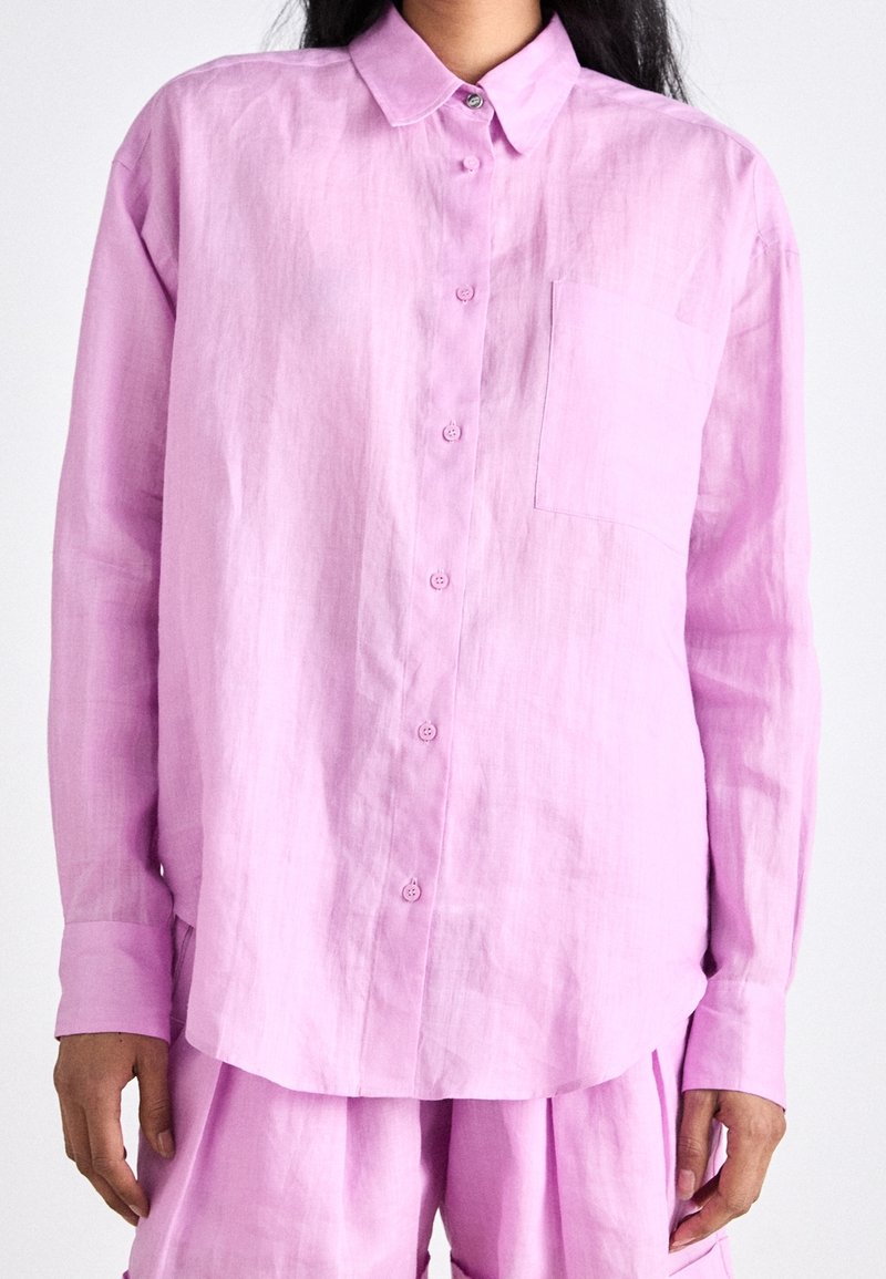 Light pink linen button-up shirt featuring a classic collar, single chest pocket, and long sleeves, paired with matching trousers.