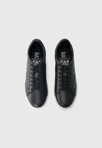 Adidași din piele neagră cu tălpi de cauciuc alb, având un design low-top și sistem clasic de șireturi. Logo-ul mărcii este vizibil pe interior.
