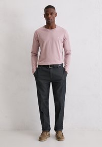 Różowa koszula z długim rękawem i okrągłym dekoltem, zestawiona z ciemnoszarymi spodniami i beżowymi butami. Prosty design z drobnym detalem w postaci logo.