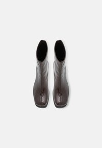 Bottines en cuir marron avec une finition lisse et brillante, bout carré et couture minimale, présentant un design lisse et sans ornement.