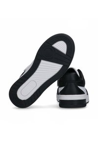 Sneaker bianche e nere con suola in gomma testurizzata, supporto per la caviglia imbottito e tomaia in pelle liscia con una fascia sul linguetta.