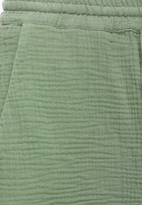 Light green cotton fabric with a textured, crinkled surface. Features a soft, elastic waistband and side pocket.