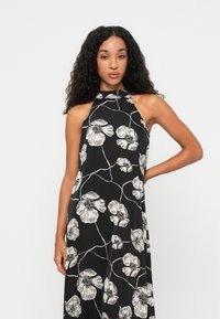 Vestido preto de alças com padrão floral branco, tecido fluido e decote alto. Apresenta um caimento relaxado e design minimalista.