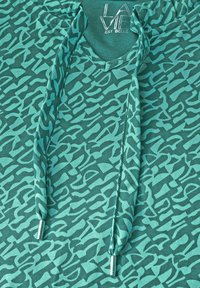 Türkisfarbener Hoodie mit einem strukturierten, abstrakten Muster in helleren Türkistönen. Beinhaltet einen V-Ausschnitt, Kordelzüge und Metallverzierungen an den Enden.