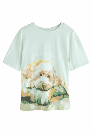 Camiseta de manga corta verde claro con una ilustración impresa de un perro descansando sobre un cojín, con el texto "Cockapooped".