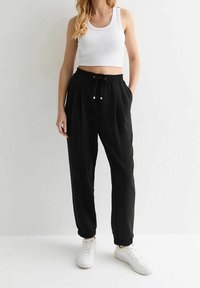 Zwarte joggerbroek met elastische boorden, een taille met trekkoord en zijzakken, gecombineerd met een wit cropped tanktop en witte sneakers.