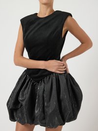 Vestido preto com um corpete justo e sem mangas em tecido suave, transicionando para uma saia volumosa e brilhante com pregas e um padrão em relevo.