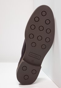 Semelle de chaussure en daim foncé avec des motifs circulaires antidérapants, marque en relief "HACKETT" et taille "41", présentant un design plat et une texture.