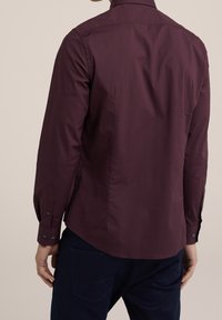 Mörk burgundy skjorta med lång ärm, knappar vid ärmslut, klassisk krage och en slät textur, med en något rundad nederkant.