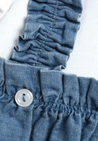 Light blue denim fabric features ruffled straps with a button detail. Texture is smooth with a slight sheen, and stitching is visible.