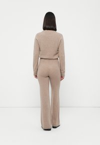 Beige gebreide twee-delige set, bestaande uit een aansluitend langmouwtop en flared broek. Zachte textuur, elastische tailleband en uniforme kleur doorheen.