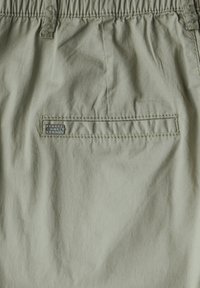 Ljusgröna tygshorts med resårmidja, med en bakficka som har en silveretikett med texten "STREET ONE STUDIO."