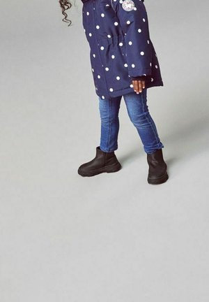 Cappotto blu navy a pois con cerniera e tasche frontali, abbinato a jeans di denim blu e stivaletti neri con suola in gomma.