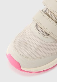 Μπεζ αθλητικό παπούτσι με επάνω μέρος από δίχτυ, που διαθέτει τρεις φαρδιές λουρίδες βέλκρο και ροζ λαστιχένια σόλα. Ομαλή υφή με ενισχυμένη μύτη.