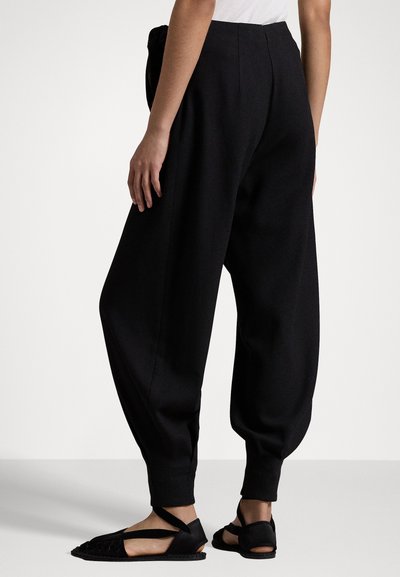 Zwarte wijde broek gemaakt van zachte stof met een hoge taille, met een taps toelopende enkel en zijzakken. Gekocht met platte zwarte sandalen.