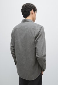 Camicia grigia in tessuto intrecciato con maniche lunghe, design con colletto, orlo curvo e polsini con bottone, che presenta una sottile trama e un tessuto leggero.