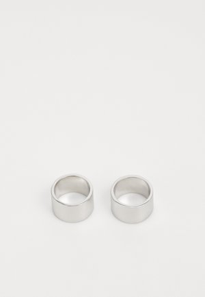 Dos anillos de plata con un acabado suave y pulido. Tienen un diseño de banda ancha y un borde superior ligeramente redondeado. Sin patrones distintivos.