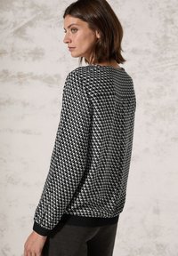 Schwarz-weiß gemusterter Sweatshirt mit Rundhalsausschnitt und langen Ärmeln. Strukturiertes Gewebe zeigt geometrische Formen. Rippenbündchen und -saum.